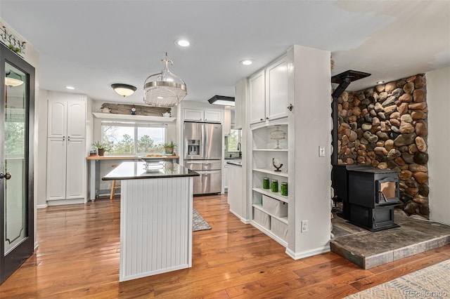 kitchen with a breakfast bar, white cabinets, hardwood / wood-style flooring, a wood stove, and stainless steel refrigerator with ice dispenser