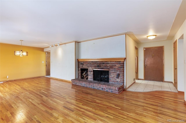 unfurnished living room featuring a brick fireplace, a notable chandelier, and light wood-type flooring