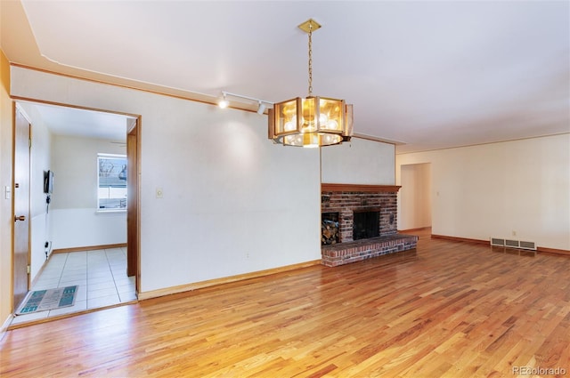 unfurnished living room featuring a brick fireplace, hardwood / wood-style flooring, a notable chandelier, and rail lighting