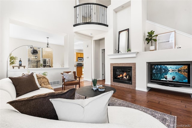 living area with visible vents, wood-type flooring, a fireplace, baseboards, and a towering ceiling