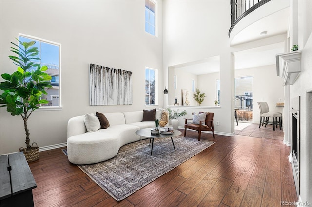 living area with hardwood / wood-style floors, a towering ceiling, baseboards, and a wealth of natural light