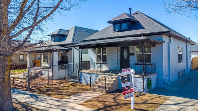 view of front of house with covered porch, brick siding, a shingled roof, and fence