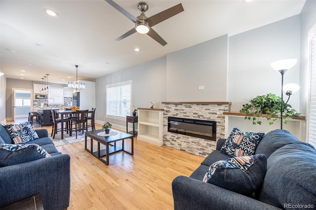 living area with a stone fireplace, recessed lighting, ceiling fan with notable chandelier, baseboards, and light wood-type flooring