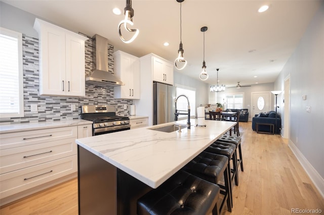 kitchen with white cabinets, wall chimney range hood, appliances with stainless steel finishes, decorative backsplash, and a center island with sink