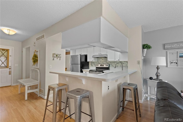 kitchen featuring tasteful backsplash, white cabinetry, a kitchen bar, kitchen peninsula, and stainless steel appliances