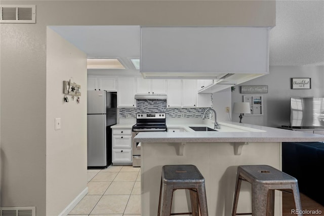 kitchen featuring light tile patterned floors, a kitchen breakfast bar, kitchen peninsula, stainless steel appliances, and white cabinets