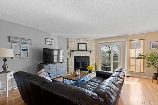 living room with a stone fireplace, light wood-type flooring, and a textured ceiling