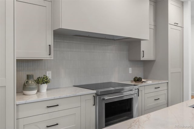 kitchen featuring tasteful backsplash, stainless steel electric stove, light stone counters, and premium range hood