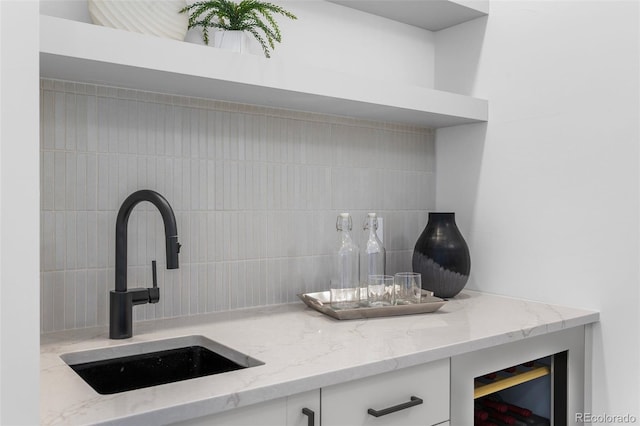 interior details featuring backsplash, light stone counters, white cabinetry, a bar, and a sink