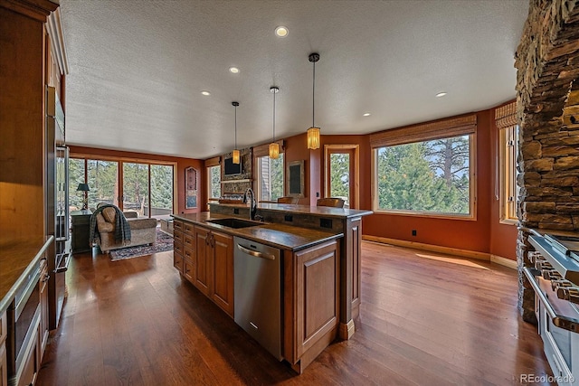 1456 Shavano Ct, Evergreen, CO 80439 - kitchen with stainless steel appliances, dark wood-style flooring, a textured ceiling, brown cabinetry, and a kitchen island with sink