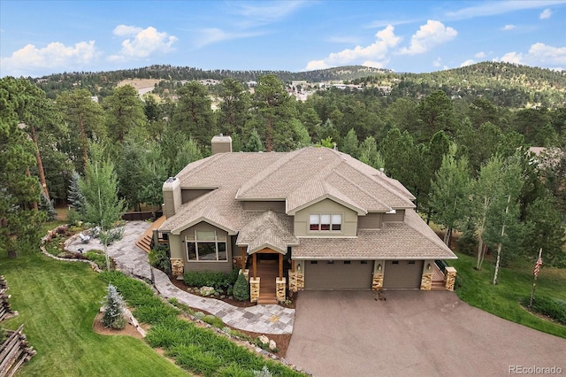 1456 Shavano Ct, Evergreen, CO 80439 - view of front of house featuring stone siding, a chimney, a garage, a wooded view, and driveway