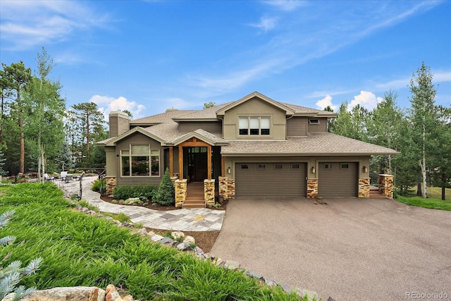 1456 Shavano Ct, Evergreen, CO 80439 - view of front of house featuring stone siding, driveway, a chimney, an attached garage, and roof with shingles