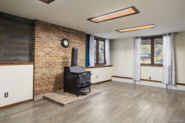 unfurnished living room featuring a wood stove, a wealth of natural light, a textured ceiling, and hardwood / wood-style flooring