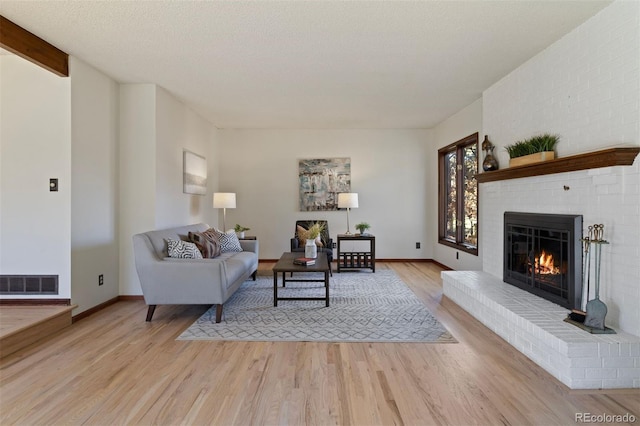 living room with beam ceiling, a brick fireplace, a textured ceiling, and light wood-type flooring