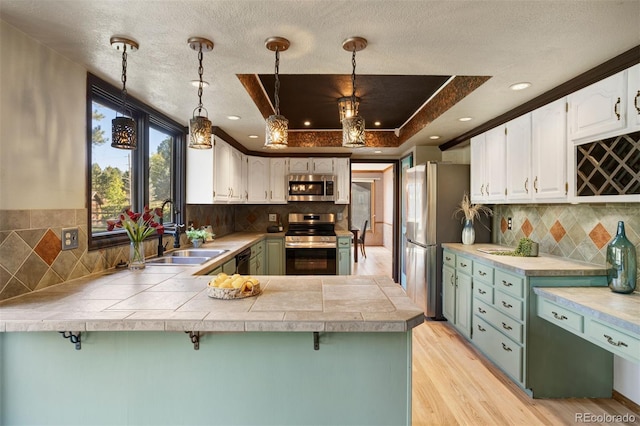 kitchen featuring a raised ceiling, kitchen peninsula, hanging light fixtures, white cabinetry, and stainless steel appliances