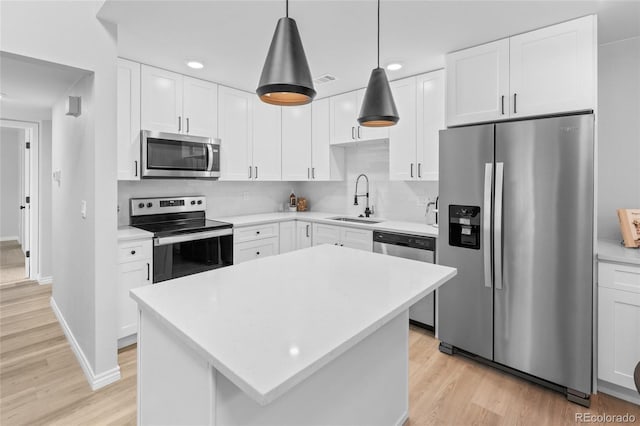 kitchen featuring stainless steel appliances, sink, decorative light fixtures, white cabinets, and a center island