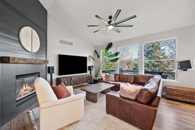 living room with a tiled fireplace, a ceiling fan, plenty of natural light, and high vaulted ceiling