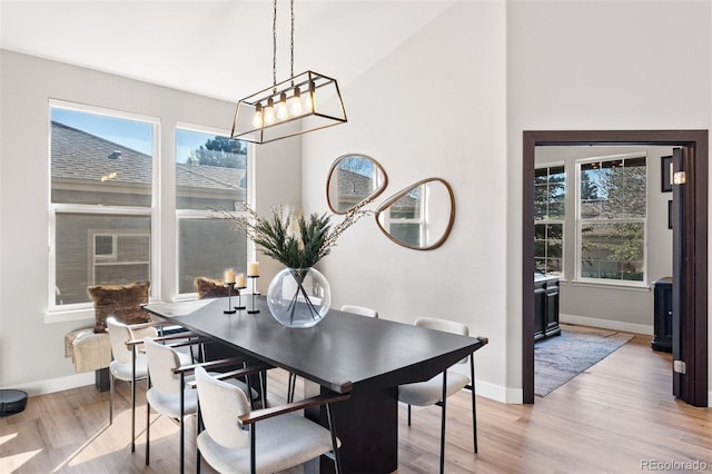 dining room featuring baseboards, light wood-style flooring, a chandelier, and vaulted ceiling