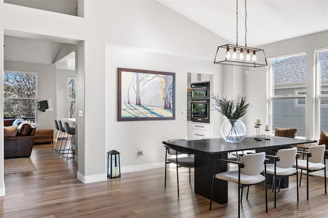 dining area featuring wood finished floors, baseboards, and high vaulted ceiling