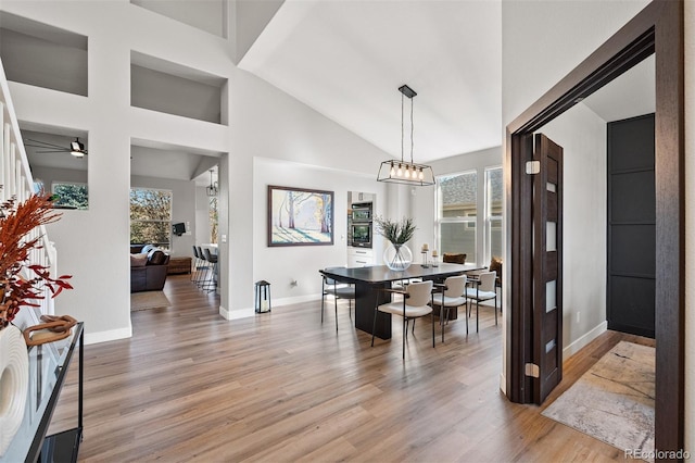dining space with light wood-type flooring, baseboards, ceiling fan, and high vaulted ceiling