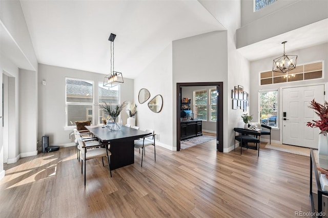 dining area featuring a chandelier, a towering ceiling, light wood-style floors, and baseboards