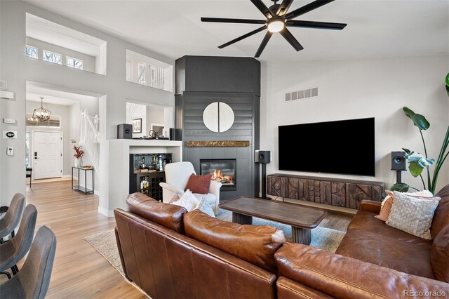 living area featuring a ceiling fan, light wood finished floors, a fireplace, high vaulted ceiling, and a chandelier