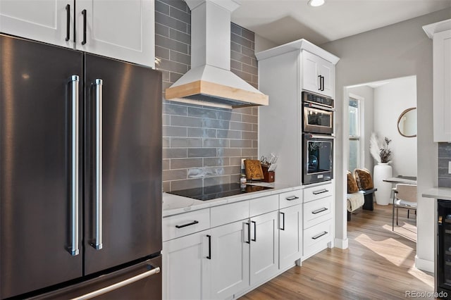 kitchen with stainless steel appliances, wall chimney range hood, tasteful backsplash, white cabinetry, and recessed lighting