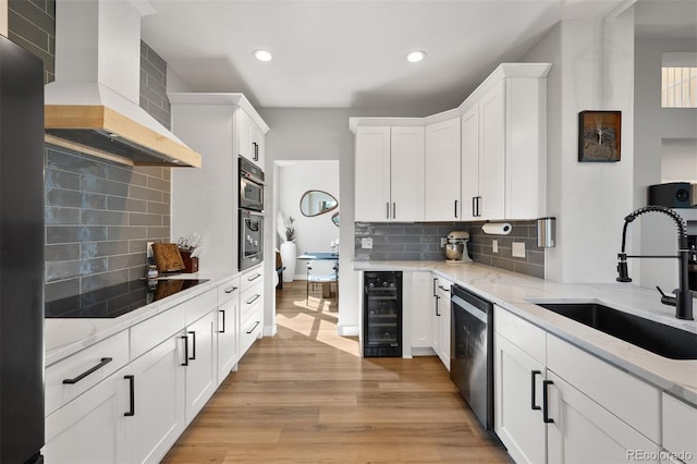 kitchen with wall chimney range hood, a sink, wine cooler, black electric cooktop, and stainless steel dishwasher
