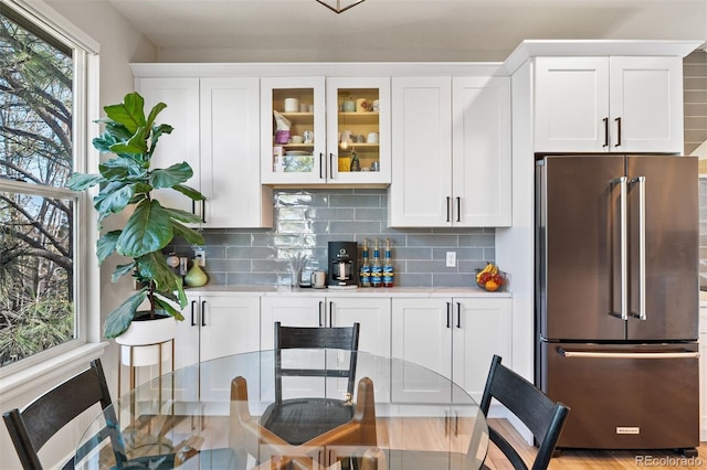 kitchen with high quality fridge, light countertops, white cabinetry, and glass insert cabinets