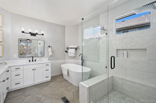 full bath with tile walls, a stall shower, vanity, a freestanding bath, and a wainscoted wall