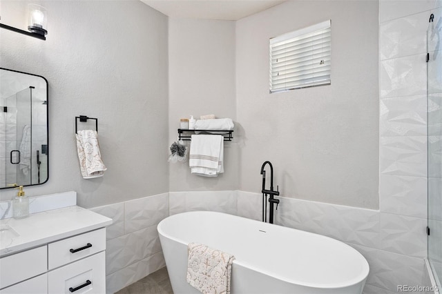 bathroom featuring tile walls, vanity, a stall shower, a freestanding tub, and a wainscoted wall