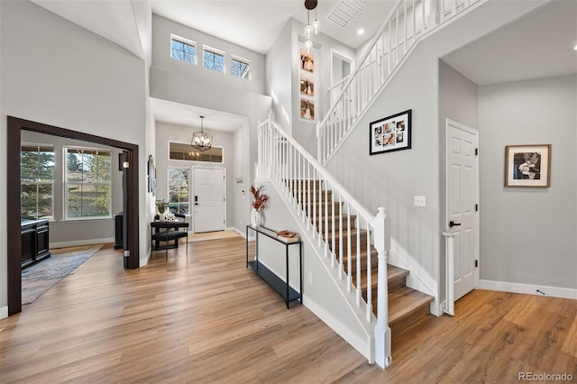 staircase with baseboards, wood finished floors, a towering ceiling, a chandelier, and recessed lighting