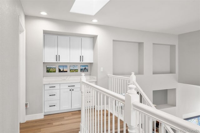 hall featuring an upstairs landing, light wood-style floors, recessed lighting, and a skylight