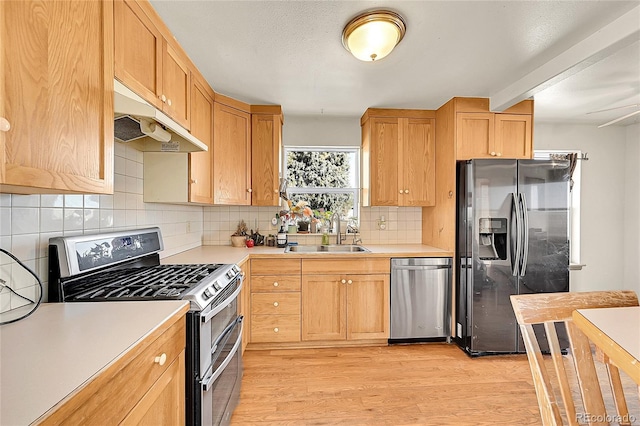 kitchen featuring a sink, under cabinet range hood, stainless steel appliances, light wood-style floors, and light countertops