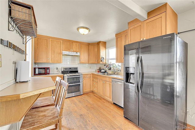 kitchen featuring under cabinet range hood, light countertops, decorative backsplash, appliances with stainless steel finishes, and a sink