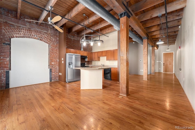 kitchen with stainless steel refrigerator with ice dispenser, black dishwasher, light wood-style floors, light countertops, and a towering ceiling