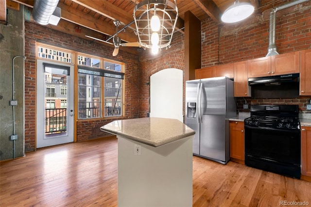 kitchen featuring black gas range, stainless steel fridge with ice dispenser, range hood, brick wall, and light wood-type flooring