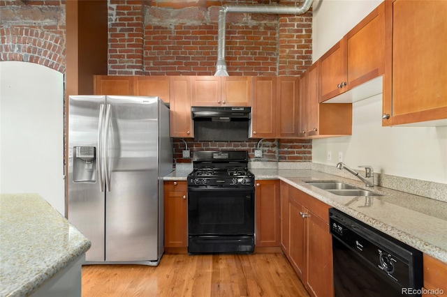 kitchen with black appliances, a sink, under cabinet range hood, light stone counters, and light wood-style floors