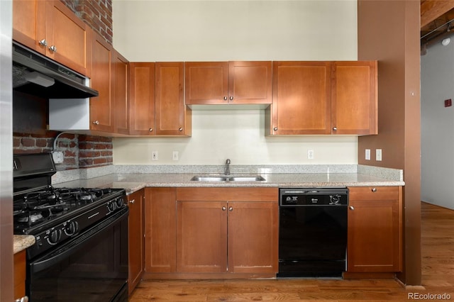 kitchen featuring black appliances, a sink, under cabinet range hood, light wood-style floors, and light stone countertops