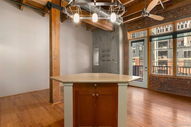 kitchen featuring brick wall, light wood-style flooring, a ceiling fan, light countertops, and a center island
