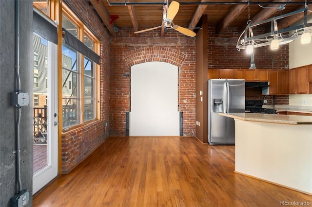 kitchen with stainless steel refrigerator with ice dispenser, black range with gas cooktop, range hood, light wood-style flooring, and brick wall