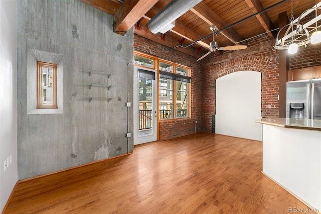 unfurnished living room featuring brick wall, wooden ceiling, wood finished floors, a ceiling fan, and a towering ceiling