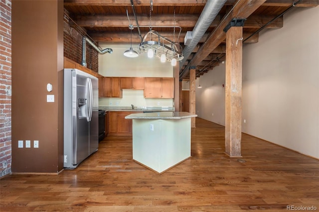 kitchen with stainless steel refrigerator with ice dispenser, a kitchen island, a towering ceiling, light wood finished floors, and brick wall