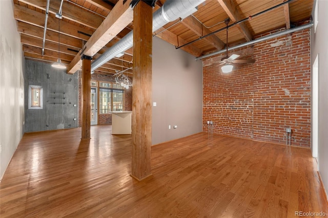 unfurnished living room with brick wall, wood finished floors, ceiling fan, beam ceiling, and wood ceiling
