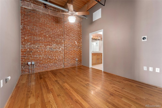 unfurnished room featuring brick wall, ceiling fan, a towering ceiling, wood finished floors, and wood ceiling