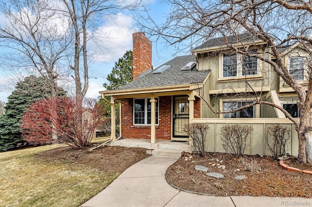 view of front of house with brick siding, covered porch, a chimney, and a shingled roof