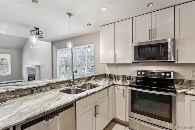 kitchen featuring a sink, light stone counters, stainless steel appliances, a stone fireplace, and white cabinets