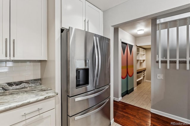 kitchen with backsplash, light stone counters, stainless steel refrigerator with ice dispenser, wood finished floors, and white cabinetry