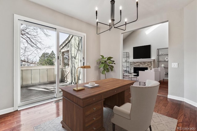 office space with baseboards, a stone fireplace, wood finished floors, and an inviting chandelier