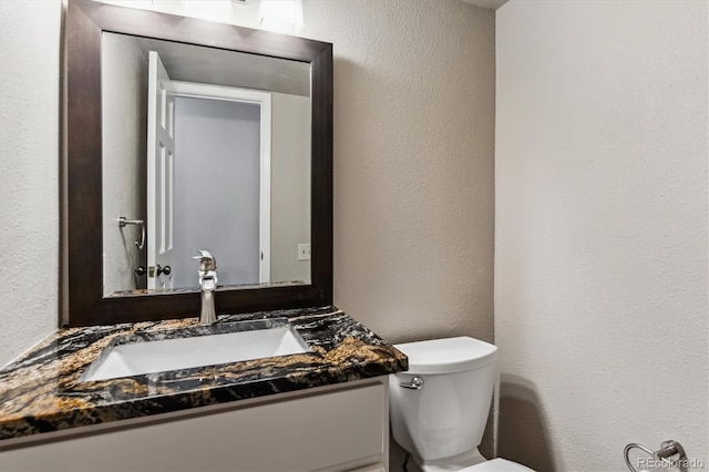 half bath featuring toilet, vanity, and a textured wall